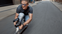 Casey Neistat crouching on Skateboard with Camera