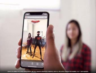 Person holding smartphone which uses augmented reality technology to project Spider-Man next to a woman standing in the background.